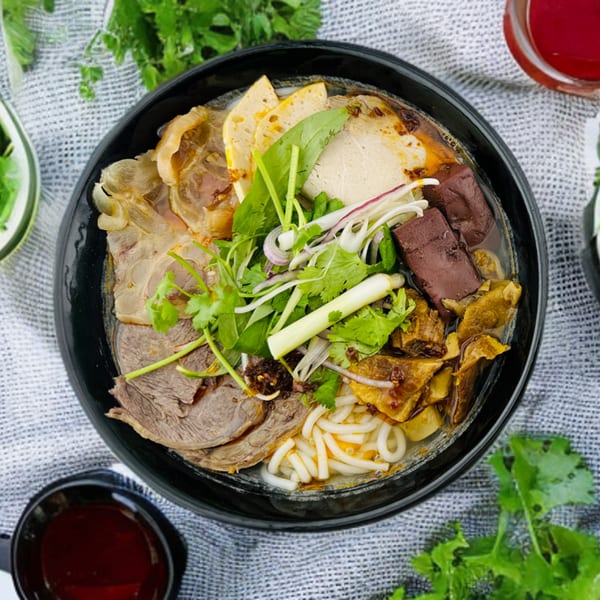 Overhead view of a Vietnamese bun bo Hue soup with various meats, noodles, and herbs.