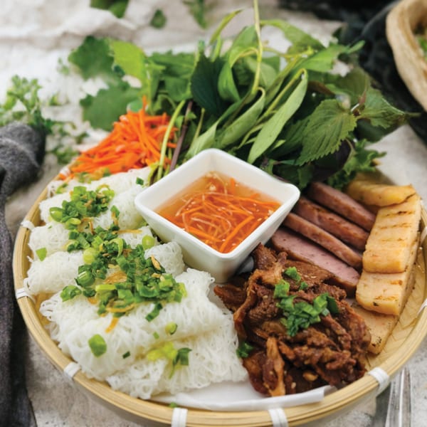 A Vietnamese platter with rice vermicelli, grilled meats, fresh herbs, shredded carrots, and dipping sauce.