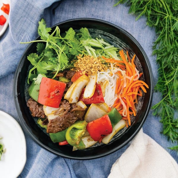 A Vietnamese vermicelli bowl with beef, bell peppers, onions, carrots, and cilantro.
